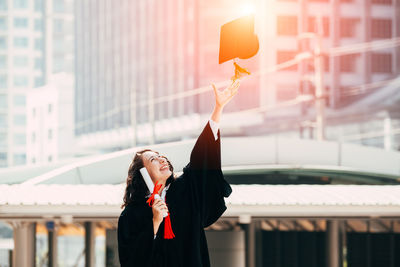 Smiling woman wearing graduation gown in city