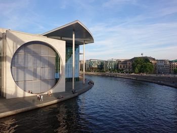 Gazebo by river in city against sky