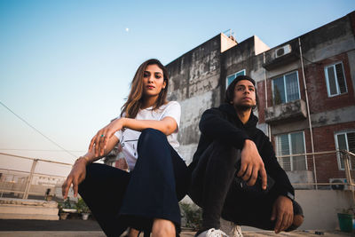 Young woman sitting in city against sky