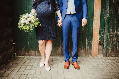 Low section of bride and groom with bouquet standing on footpath