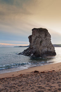 Rock formation on beach against sky during sunset