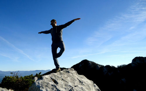 Low angle view of a young man jumping against blue sky