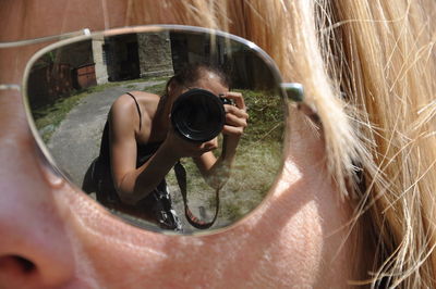 Cropped image of eye wearing sunglasses with reflection of woman photographing through camera