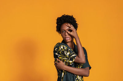 Young african american woman with short hair dressed in a summer shirt posing on an orange colored