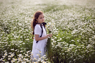 Portrait girl child in a white dress stands on a camomile field. bouquet of flower