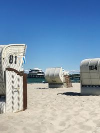 Hooded chairs on beach against clear blue sky