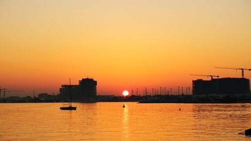 Silhouette buildings by sea against romantic sky at sunset