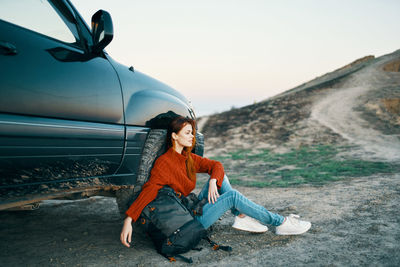 Full length of woman sitting on car against sky