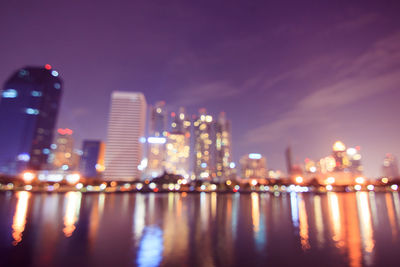 Illuminated buildings by river against sky at night