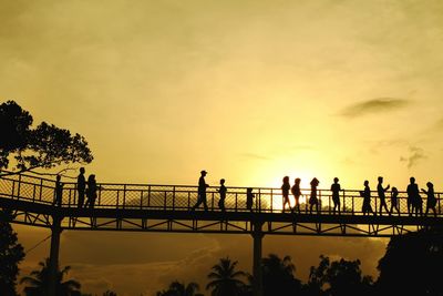 Silhouette people on bridge against sky during sunset