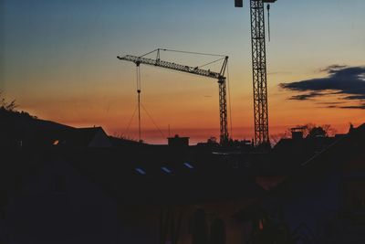 Silhouette crane by building against sky during sunset
