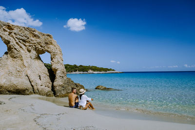 Man sitting on rock by sea against sky