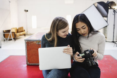 Female bloggers watching photographs on digital camera in office