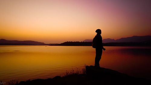Silhouette man standing on rock by sea against orange sky