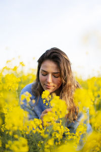 Beautiful young woman smelling yellow flower in field