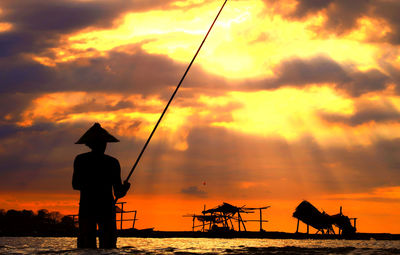 Silhouette man fishing in sea against sky during sunset