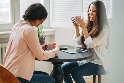 Smiling female colleagues having coffee while sitting at table