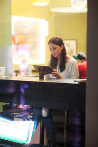Mid adult woman using digital tablet while siting in cafe seen through window