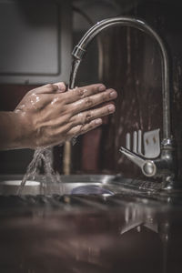 Cropped hand by faucet in kitchen