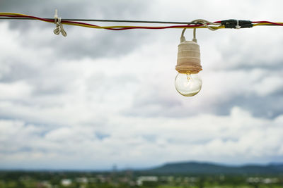 Low angle view of illuminated light bulb against cloudy sky
