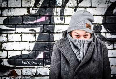 Portrait of man covering face with warm clothing while standing against wall