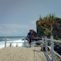 Man standing on railing by sea against sky