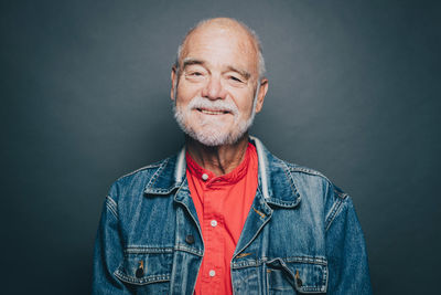 Portrait of smiling senior man wearing denim jacket against gray background