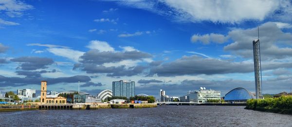 View of buildings by river against cloudy sky