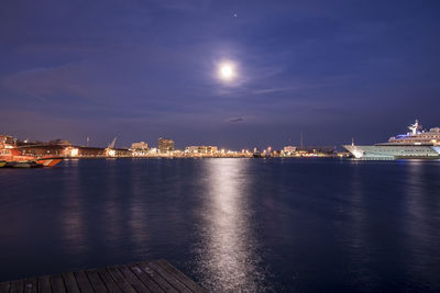 Pier over river against illuminated cityscape during night