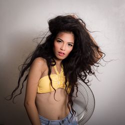 Portrait of beautiful young woman with electric fan standing against wall