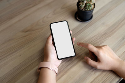 Cropped hands of woman using mobile phone on table