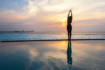 Silhouette person standing at swimming pool against sky during sunset