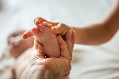 Cropped hand of woman hand and sibling hand holding newborn baby foot