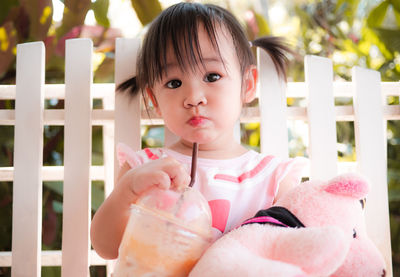 Portrait of cute baby girl drinking smoothie against fence