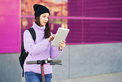 Woman holding smart phone while standing against pink wall