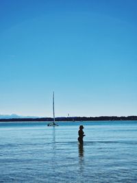 Rear view of woman standing at beach against clear blue sky