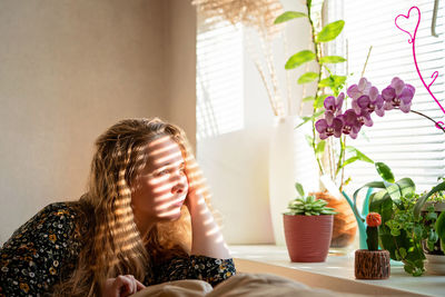 Woman looking at potted plant at home. portrait of woman sitting in front of the window at home