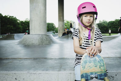 Portrait of girl with skateboard sitting at park