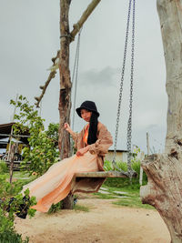 Woman sitting on tree trunk against sky