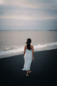 Rear view of woman walking on beach against sky