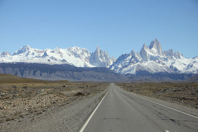 Road leading towards snowcapped mountains against clear sky