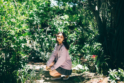 Portrait of young woman sitting against plants