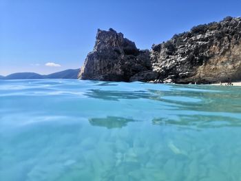 Rock formation in sea against clear blue sky