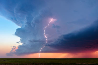 A vivid lightning bolt strikes from a towering supercell storm at sunset near briggsdale, colorado.