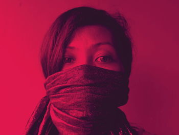 Close-up portrait of young woman covered with scarf against red background