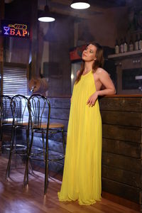 Portrait of smiling young woman standing against yellow wall