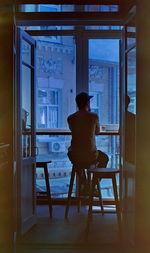 Rear view of man sitting on stool against window in cafe