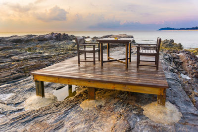 Empty wooden chairs and table on jetty against sea