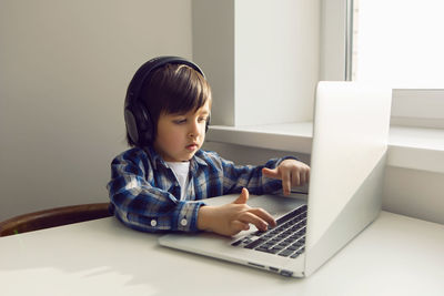 Boy child sits at a table near the window with a laptop and communicates with relatives