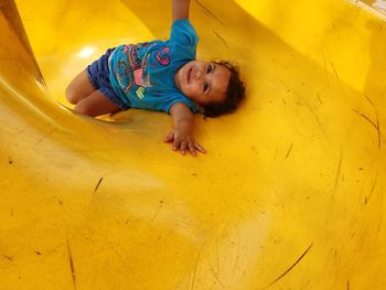 High angle view of little girl lying on slide at playground